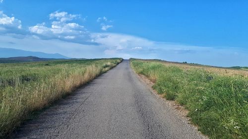 Road amidst field against sky