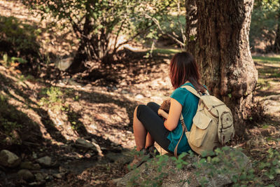 Rear view of mother sitting with daughter by tree trunk