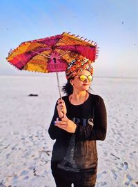 Young woman holding umbrella while standing by sea against sky