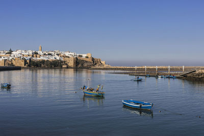 Boats moored on sea against clear blue sky