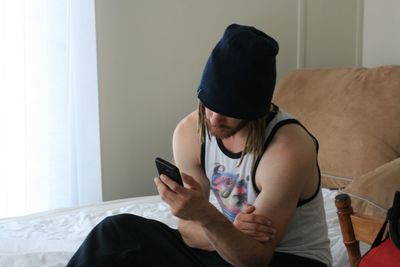 Man in cap using mobile phone on bed at home