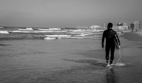 Rear view of man with surfboard walking at beach