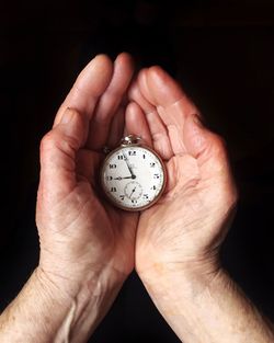 Cropped image of hand holding clock over black background