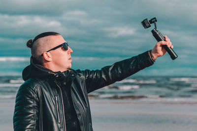 Young man with arms outstretched standing by sea against sky