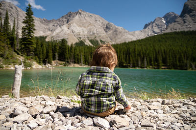 Baby sitting on rocks next to a lake in the mountains on a sunny summer day
