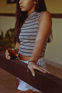 Midsection of teenage girl holding drink while standing by wood