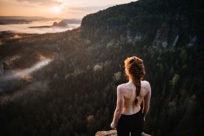 Rear view of shirtless woman standing against mountain