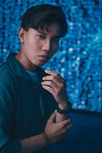 Close-up portrait of young man standing against blue lights