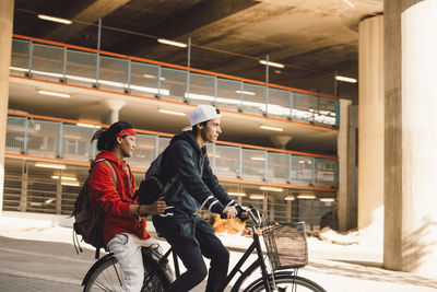 Side view of young man riding bicycle with friend in city