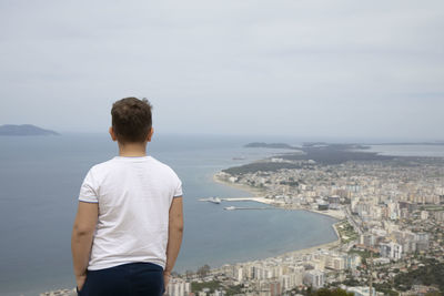 Rear view of man looking at cityscape against sky