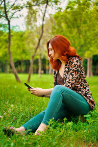 Young woman using smart phone while sitting on grass