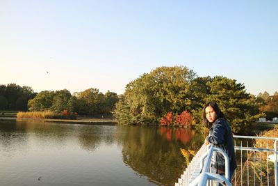 Woman sitting on bicycle by lake against clear sky