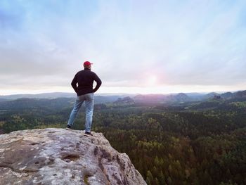 Man in jeans black outdoor sweatshirt and red cap. melancholy misty day in sandstone mountains