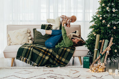 Mom and baby are having fun and playing on the sofa in the apartment decorated for christmas. 