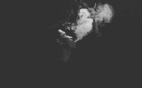 Side view of man smoking cigarette against black background