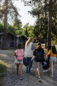 Rear view of camp counselor walking with girls on footpath at summer camp