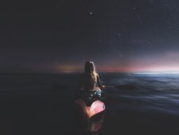 Rear view of woman kayaking at sea against star field