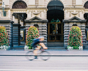 Woman riding bicycle on street against building