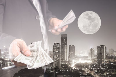 Double exposure of businessman standing against modern illuminated buildings in city