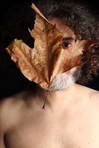 Portrait of shirtless man with autumn leaf on face against black background