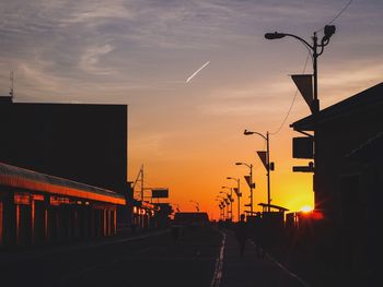 Road by silhouette street against sky at sunset