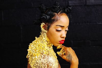 Side view of shirtless female model with golden glitters by black wall