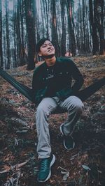 Portrait of young man sitting on tree trunk in forest