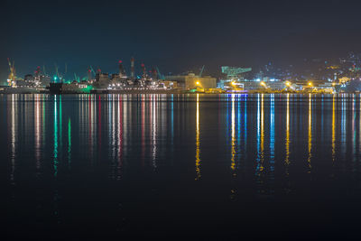 Illuminated city by sea against sky at night