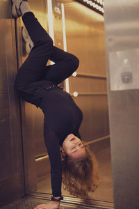 Young woman doing handstand at door of elevator