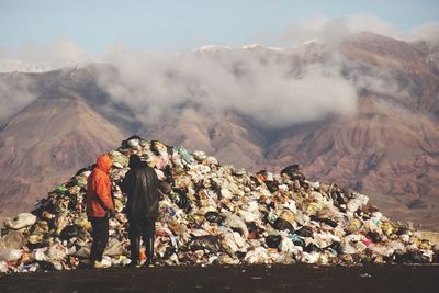 People standing in front of garbage against rocky mountains