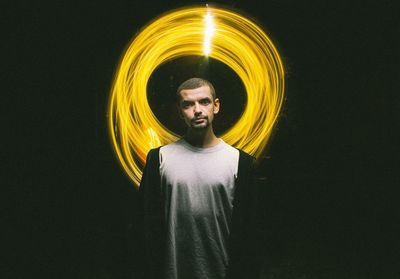 Portrait of young man standing against spinning illuminated lighting 