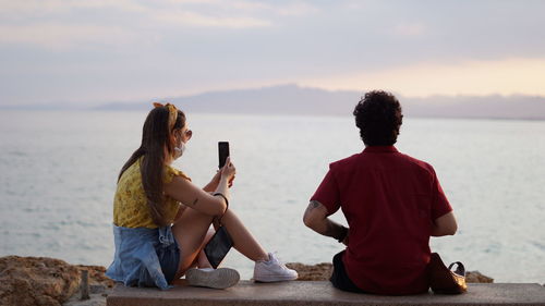 Rear view of people photographing sea against sky during sunset