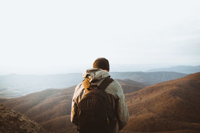 Rear view of man standing on mountain against clear sky