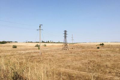 Electricity pylon on field against clear blue sky