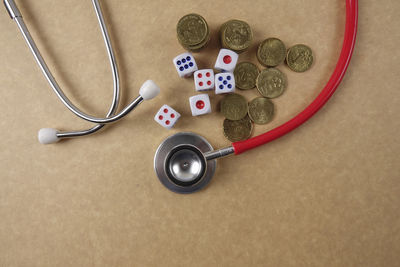 Directly above shot of stethoscope with dices and coins on brown table