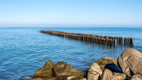 Wooden posts in sea against clear sky