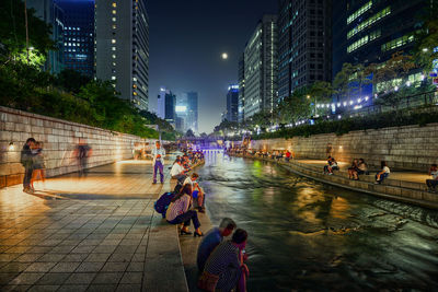 People siting by canal in city at night