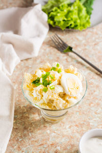 Potato salad with boiled egg, green onion and mayonnaise in a bowl on the table. vertical view