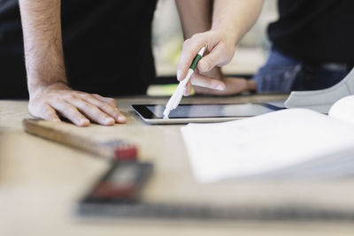 Midsection of trainee and teacher using digital tablet at table