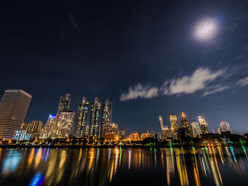 Illuminated buildings by river against sky at night