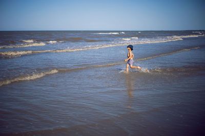 Boy child runs along the beach sea in summer in a panama hat and striped shorts