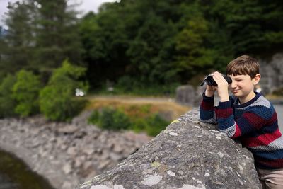 Boy looking through binoculars by retaining wall