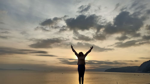 Rear view of silhouette woman standing in sea against sky