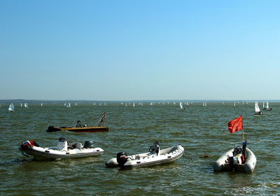 People on boats in sea against clear sky