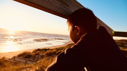 Boy looking at sea through railing during sunset