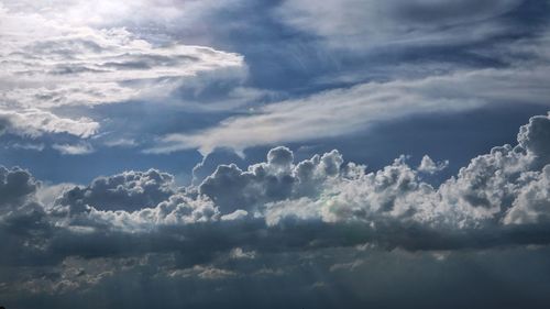 Low angle view of sunlight streaming through clouds