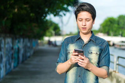 Young man looking away while standing on mobile phone