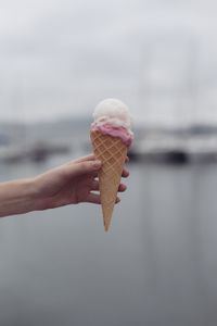 Close-up of hand holding ice cream against sea