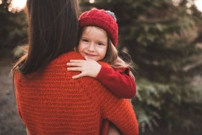 Cute smiling child girl 3-4 year old on mother hands wear knit hat and sweater outdoor.