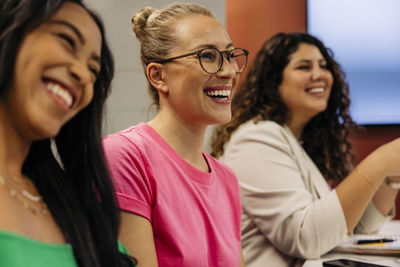 Happy businesswomen laughing with female colleagues during meeting at office